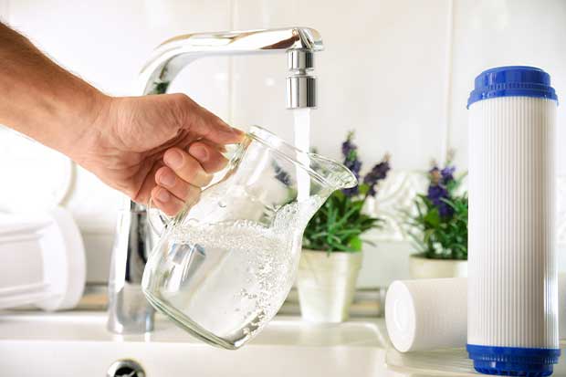 Person in the kitchen holding a jar filled with clear water that just had water treatment services in Calgary, AB