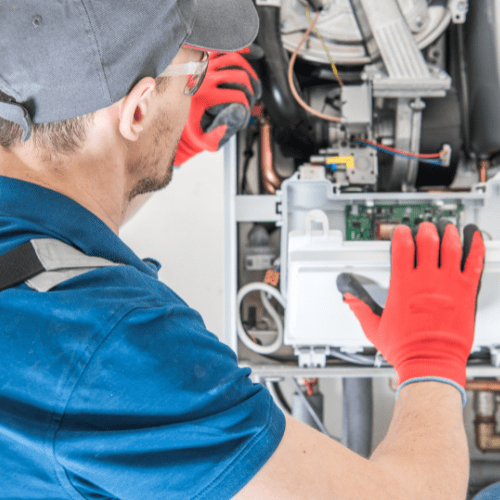 Technician in blue shirt and red gloves repairing a furnace in a residential home provided by ProStar.