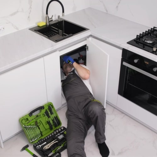 Prostar Plumbing crew checking a kitchen sink cabinet, with tools spread out beside him.