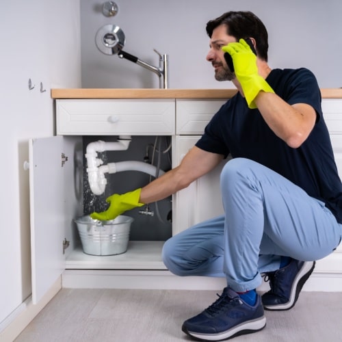 Prostar Plumbing crew in gloves checking a sink with a bucket under pipes.