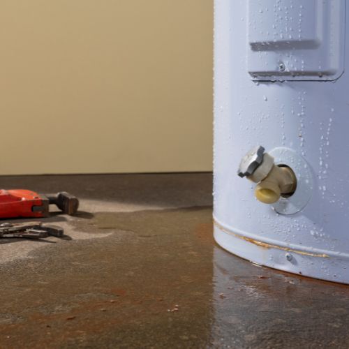 Fixing water heater leaking on a concrete floor with tools nearby by Prostar Plumbing.