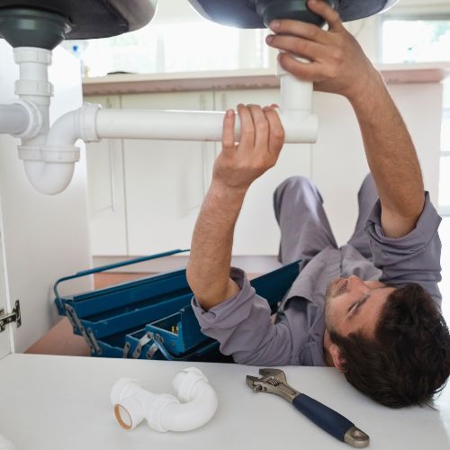 Plumber under the sink in a process of plumbing repair in Calgary, AB