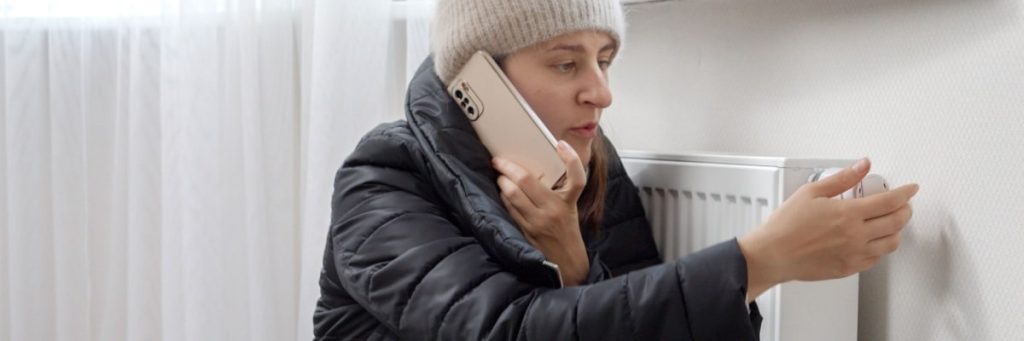 Person in winter jacket adjusting a thermostat on a wall in Calgary.