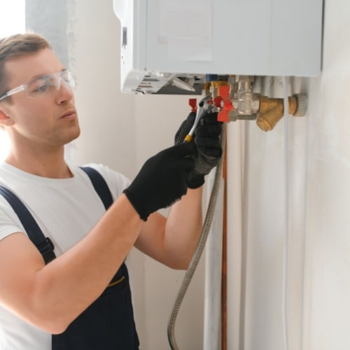 Technician in overalls repairing a wall-mounted boiler in Calgary.