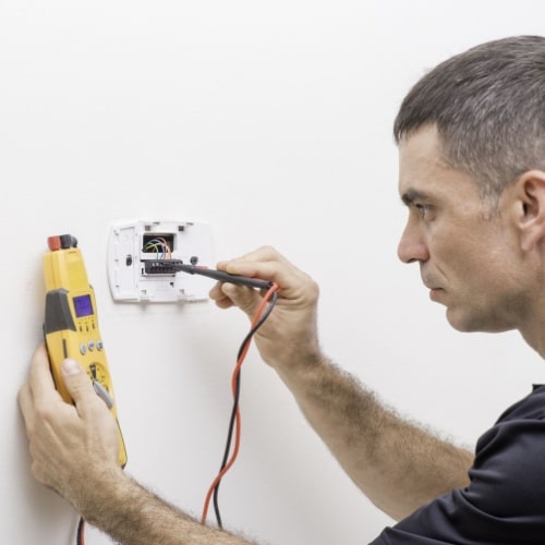 A person using a multimeter to check an electrical outlet on a wall in Calgary.