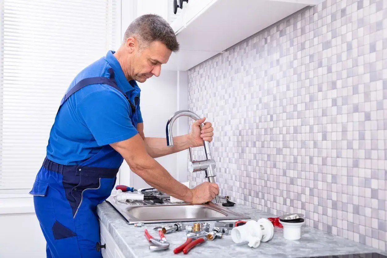 Professional plumber installing a new chrome faucet and kitchen sink.